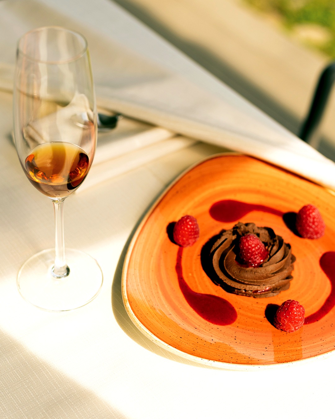 Mousse al cioccolato con lamponi su piatto in ceramica arancione, accanto a un calice di vino da dessert, al Chalet nel Parco